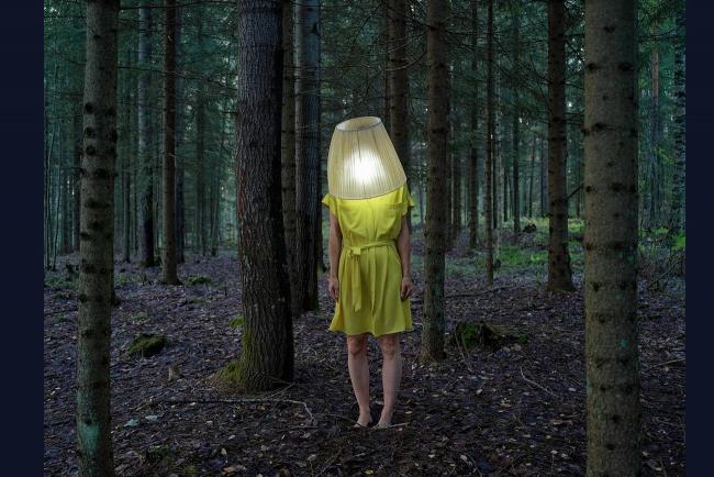 Femme en jaune dans une forêt, un abat jour éclairé à la place de la tête