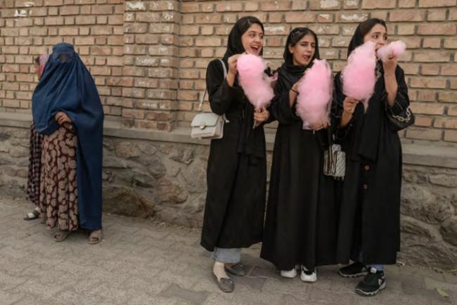 3 jeunes femmes en hidjab et abaya noires mangeant de la barbe à papa rose. En arrière plan, une femme portant 